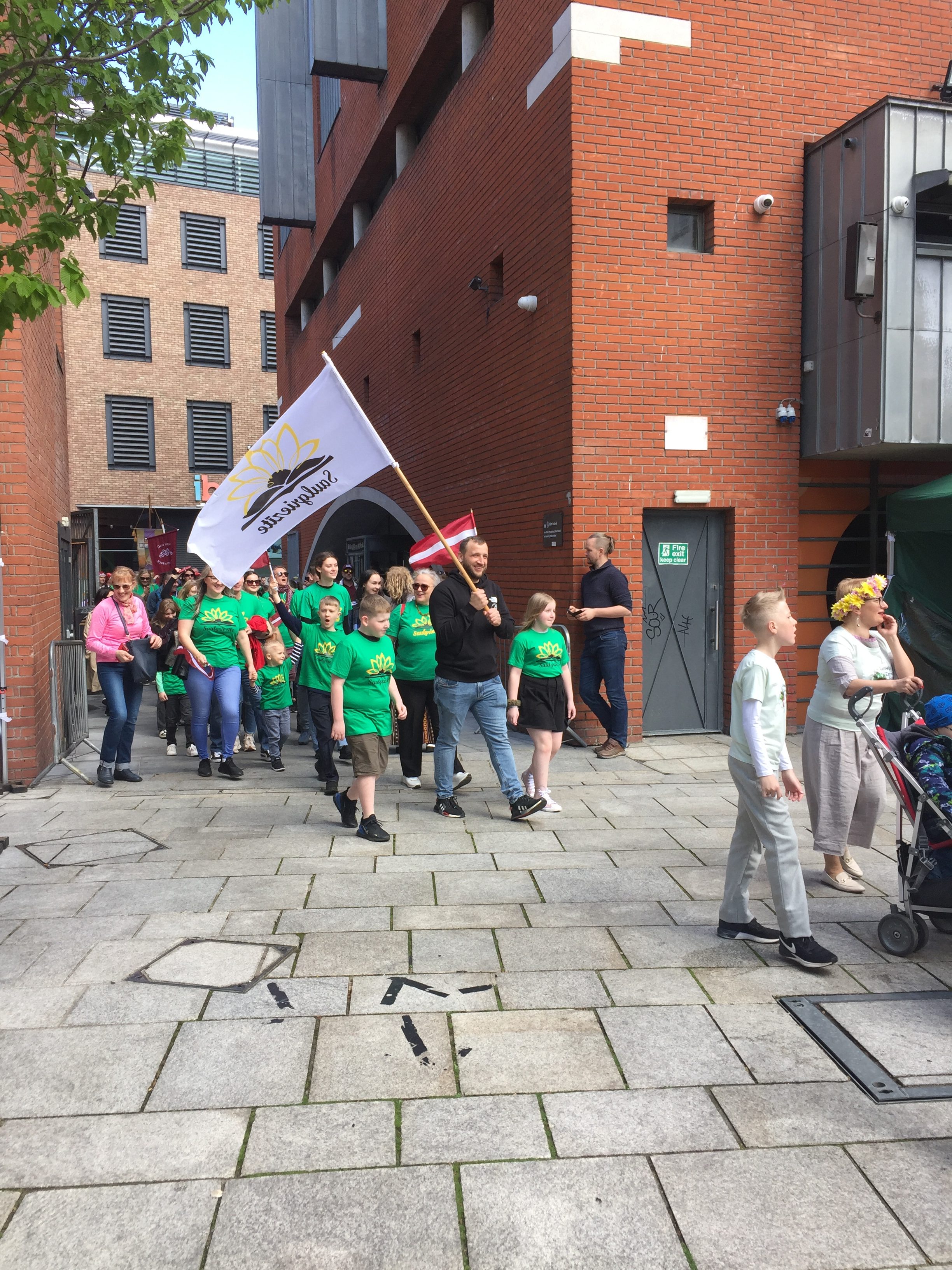 Attēls no svētkiem = bērni zaļos kreklos kopā ar Latvijas karogu dodas gājienā.