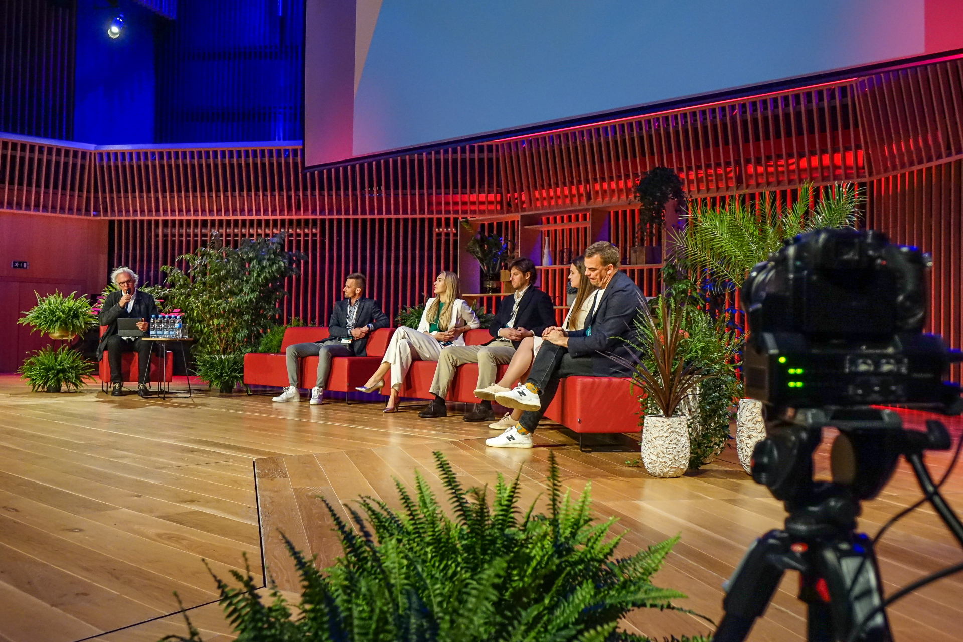 Kurzemes biznesa foruma paneļdiskusija - uz skatuves redzasm diskusijas vadītājs un 5 paneļdiskusijas dalībnieki, kas sēž rozā krēslos.